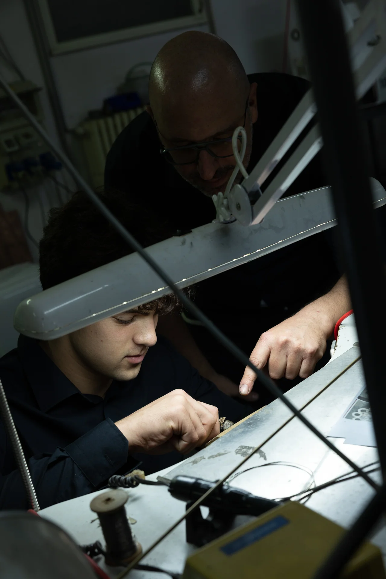Maestro orafo che guida un giovane artigiano durante la lavorazione di un gioiello